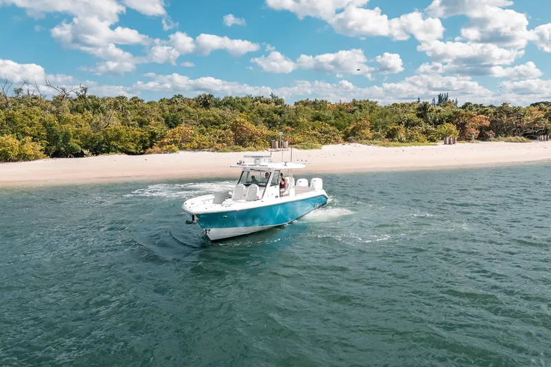 Slide: The Image of 2022 Everglades 395cc boat cruising near a sandy beach under a blue sky. - 16