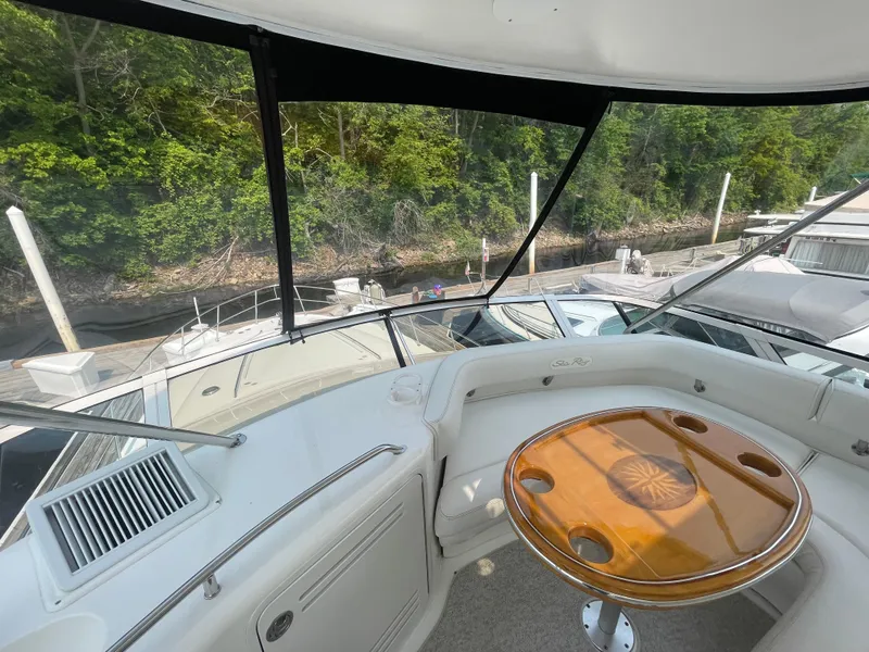 Slide: The Image of 2001 Sea Ray 480 Sedan Bridge yacht interior with wooden table and seating, docked near lush greenery. - 19