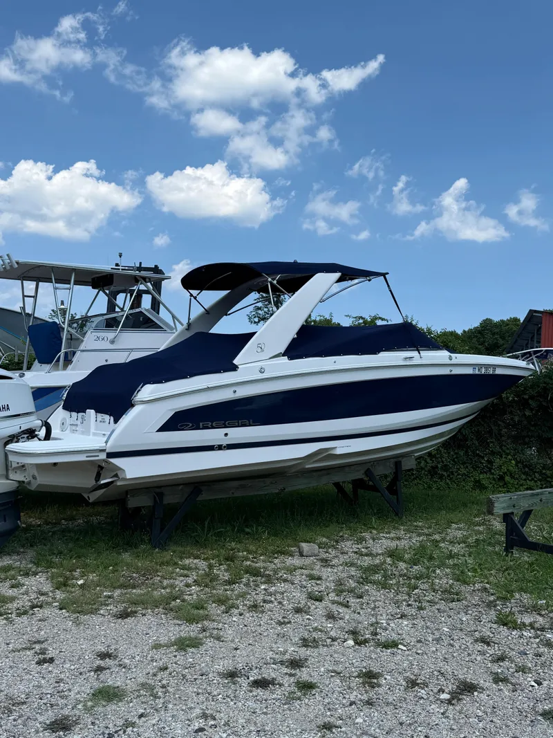The Image of 2020 Regal 26 OBX boat with blue cover, parked on grass under a clear sky. - 0