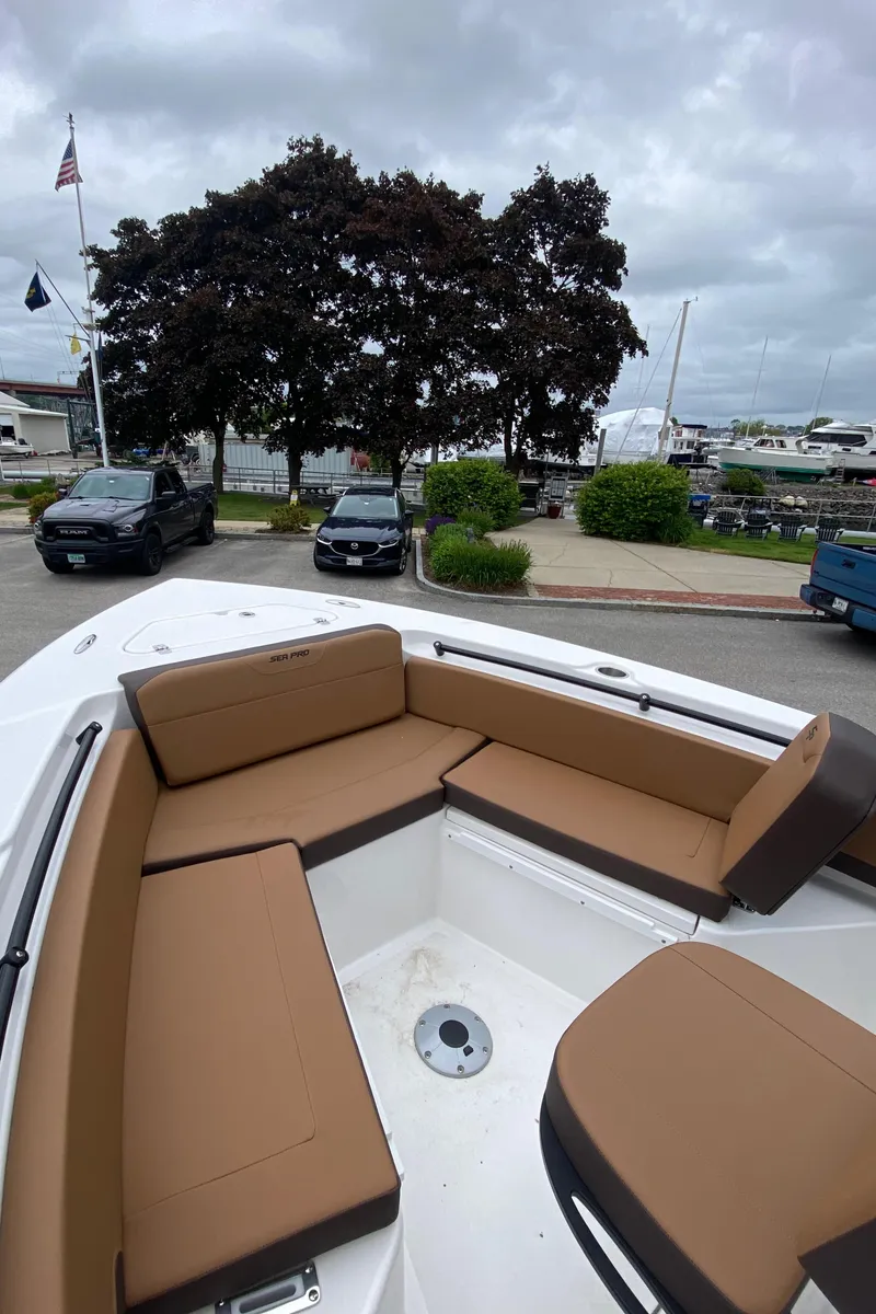 Slide: The Image of 2025 Sea Pro 225 Sandbar boat with brown seating, docked near trees and parked cars. - 11
