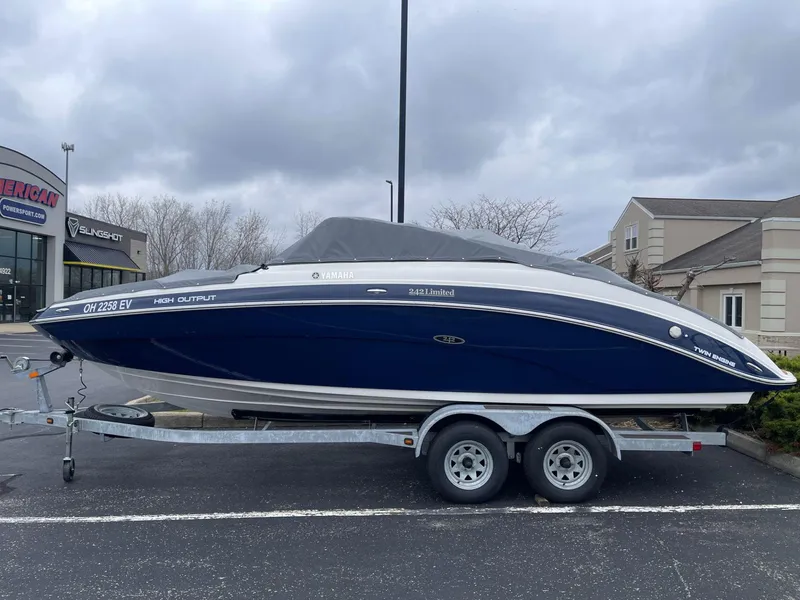 Slide: The Image of 2011 Yamaha Boats 242 Limited on trailer, parked outside dealership under cloudy sky. - 4