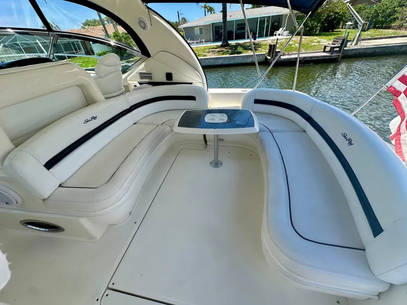Slide: The Image of 2005 Sea Ray 420 Sundancer boat interior with white seating and table, docked by water. - 7