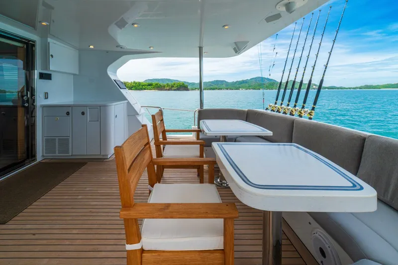 Slide: The Image of Luxurious 2002 Queenship 98 Yachtfish deck with seating, tables, and fishing rods, overlooking serene ocean. - 5