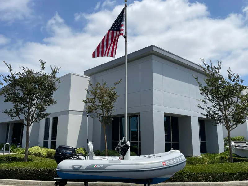 Slide: The Image of 2013 AB Inflatables Lammina 10 AL boat on trailer, parked outside modern building with American flag. - 12