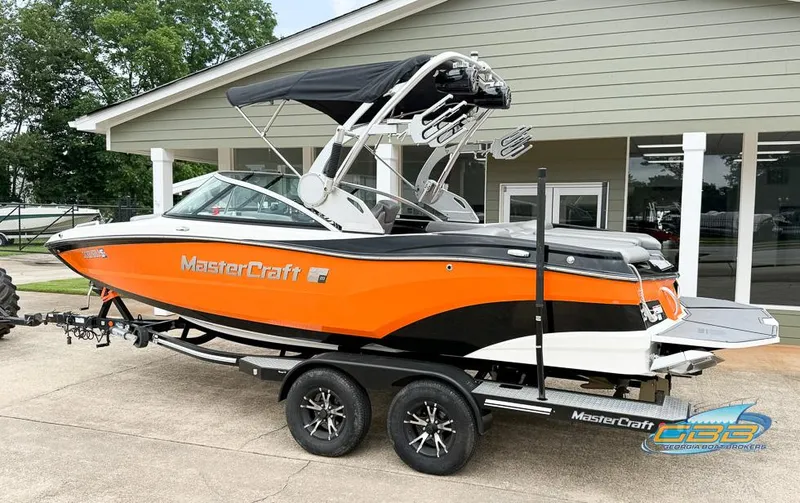 Slide: The Image of 2017 MasterCraft XT20 boat in vibrant orange on a trailer outside a building. - 2