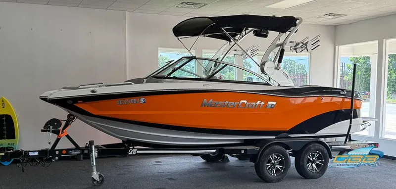 Slide: The Image of 2017 MasterCraft XT20 boat in showroom, orange and black design, on trailer. - 22
