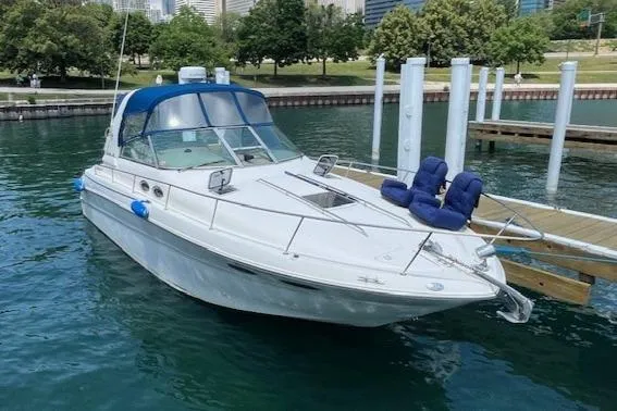 The Image of 2000 Sea Ray 310 Sundancer docked in a marina, surrounded by calm water and greenery. - 0