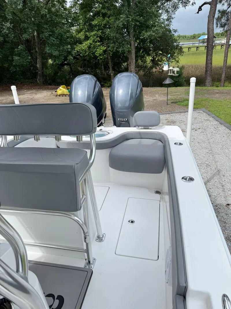 Slide: The Image of 2023 Contender 24 Sport boat interior with dual engines, gray seating, and lush greenery background. - 12