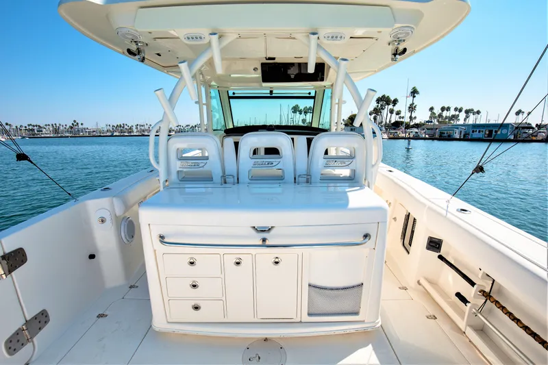 Slide: The Image of 2014 Boston Whaler 370 Outrage boat interior with seating and storage, docked by palm trees. - 15