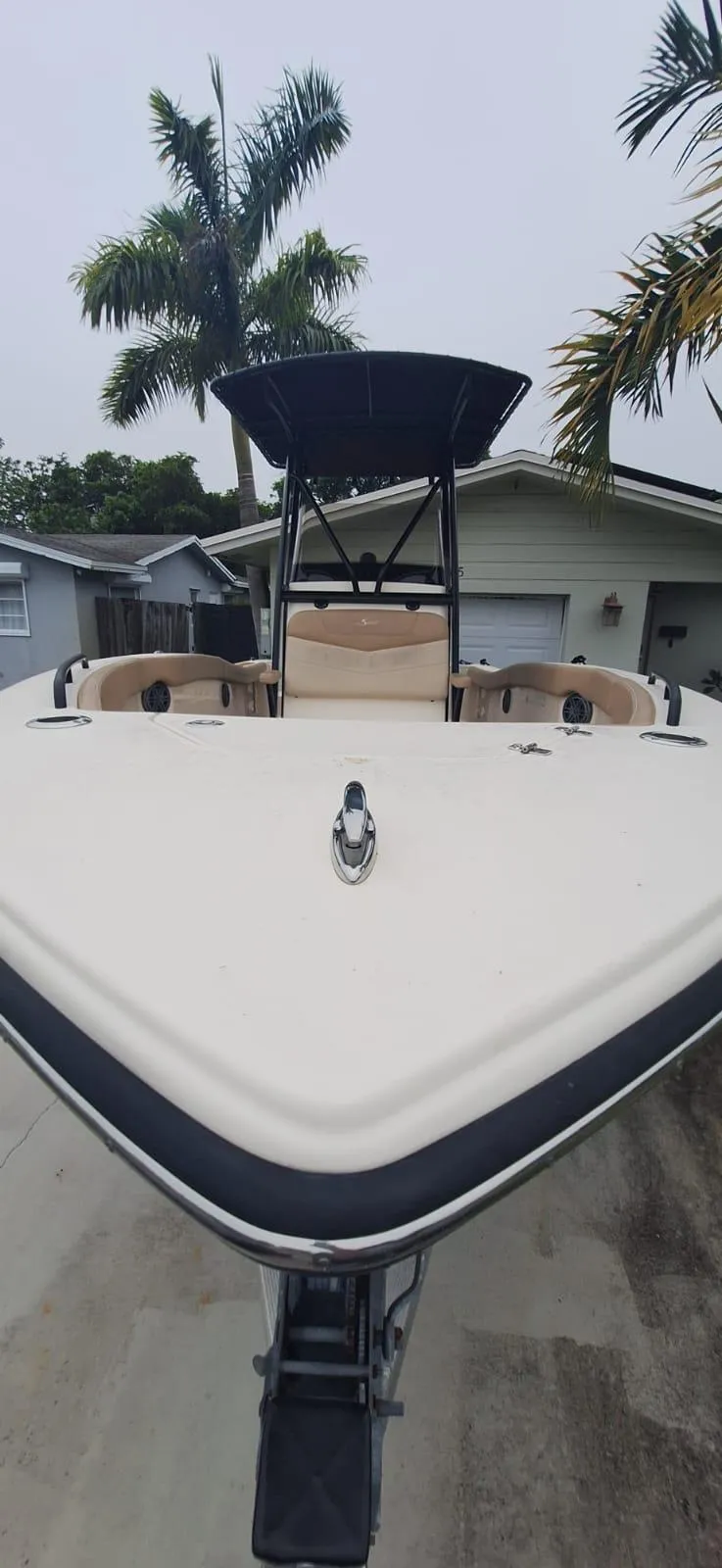 Slide: The Image of 2022 Scout 215 XSF boat with T-top, parked in a driveway, surrounded by palm trees. - 2