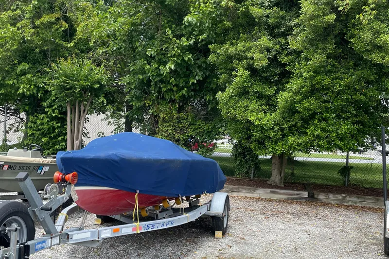Slide: The Image of Covered Alsberg Brothers 17 boat on trailer, surrounded by lush greenery. - 15