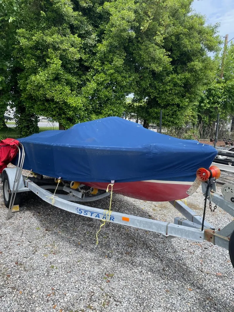Slide: The Image of Covered Alsberg Brothers 17 boat on trailer, parked outdoors, surrounded by greenery. - 2