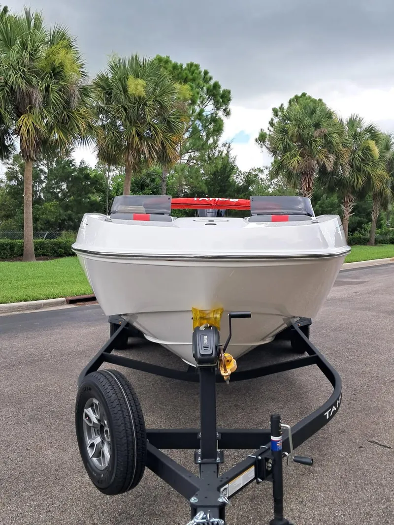 Slide: The Image of 2025 Tahoe T21 boat on trailer, parked near palm trees under cloudy sky. - 2