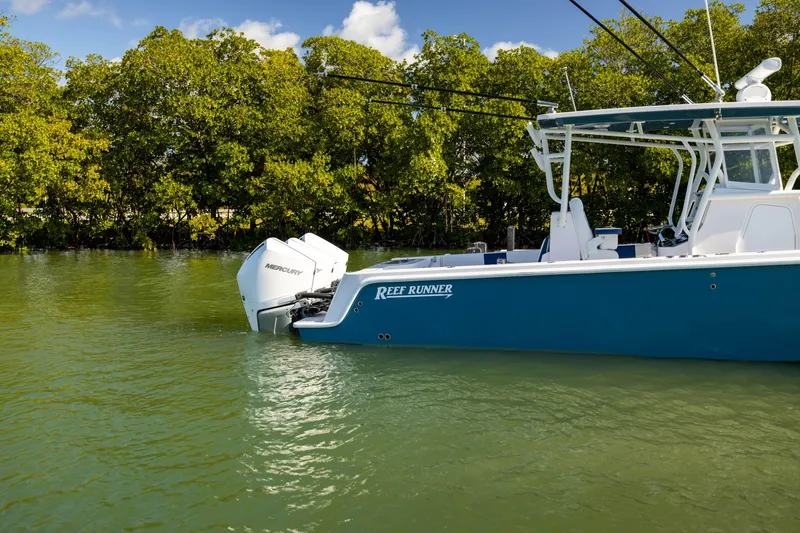 Slide: The Image of 2026 Reef Runner 340 boat with Mercury engine on calm water, surrounded by lush greenery. - 7