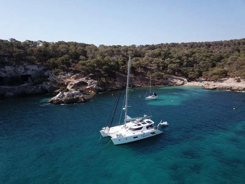 The Image of Sailing yacht Knysna 500SE 2026 anchored in a serene, turquoise bay with lush greenery. - 0