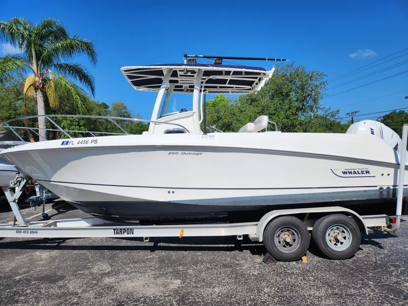 The Image of 2014 Boston Whaler 250 Outrage boat on trailer, parked outdoors under clear blue sky. - 0