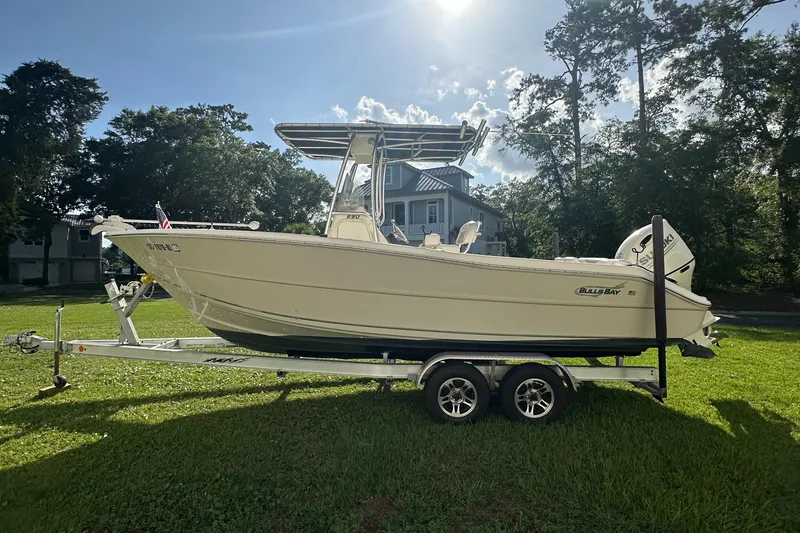 Slide: The Image of 2019 Bulls Bay 230 Center Console boat on trailer, parked on grass with trees in background. - 0