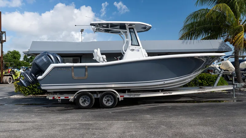 The Image of 2026 Tidewater 256 CC Adventure boat on trailer, parked outdoors near palm tree. - 0