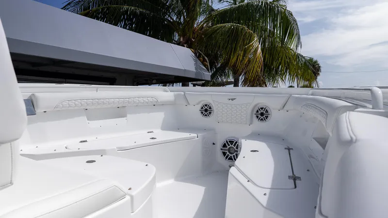 Slide: The Image of 2026 Tidewater 256 CC Adventure boat interior with white seating and speakers, under palm trees. - 21