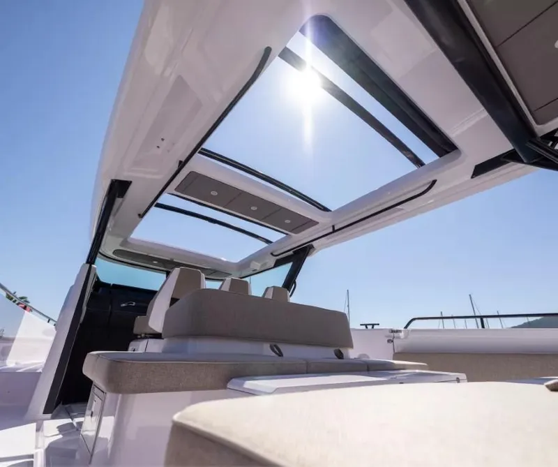 Slide: The Image of 2025 Axopar 45 Cross Top boat interior with sunroof and seating under clear blue sky. - 9