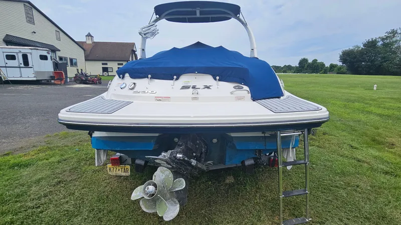 Slide: The Image of 2016 Sea Ray 230 SLX boat with blue cover, parked on grass near a building. - 4