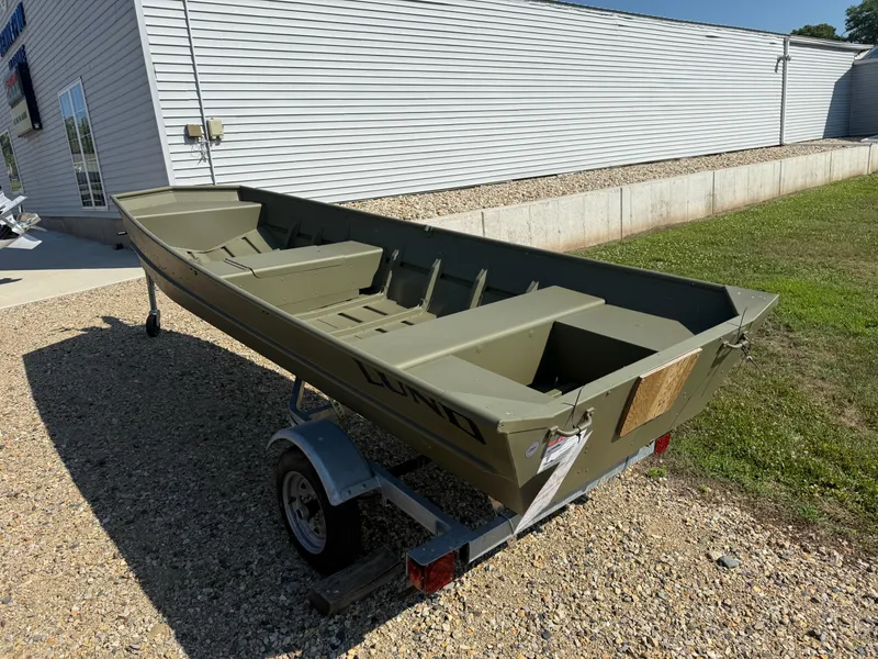 Slide: The Image of 2025 Lund 1440M boat on trailer, parked outside a building on gravel. - 3