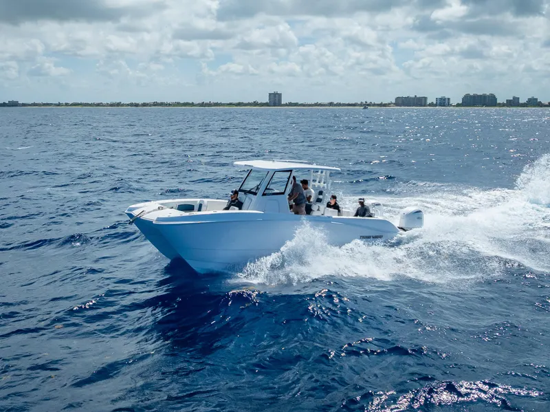 Slide: The Image of 2026 Twin Vee 260 GFX2 CC cruising on ocean near coastal buildings under cloudy sky. - 9