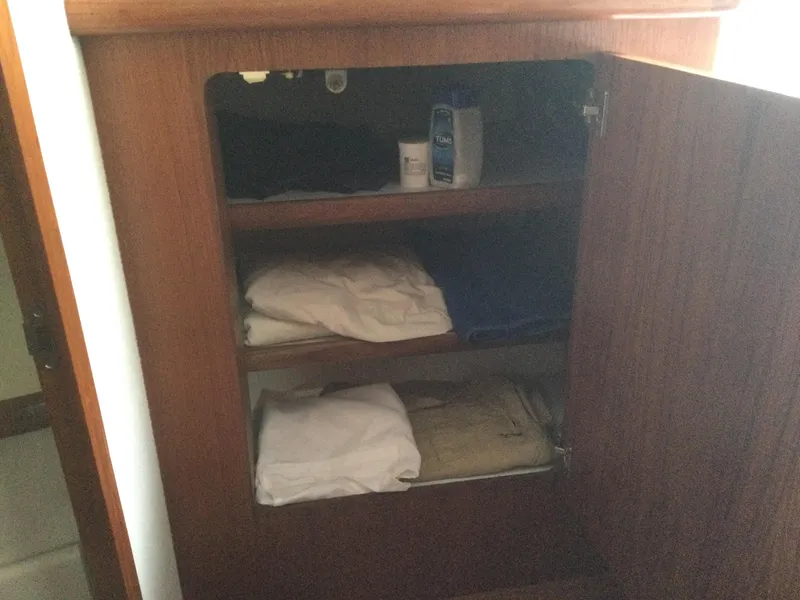 Slide: The Image of Open wooden cabinet with folded clothes and toiletries inside, on a 1995 Carver 430 Cockpit Motor Yacht. - 32
