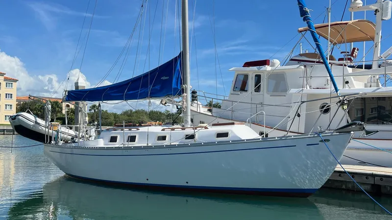 The Image of 1976 Endeavour 32' Sloop docked in a sunny marina, featuring a blue sail. - 0