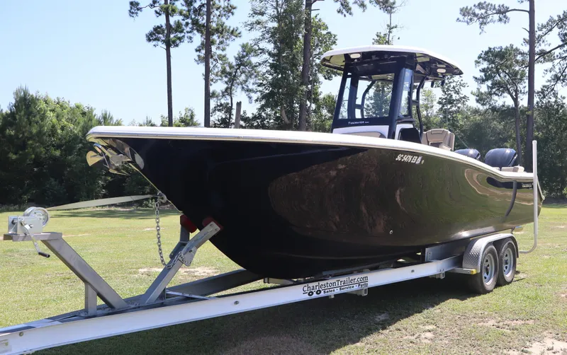 Slide: The Image of 2022 Tidewater 272 LXF boat on trailer, parked on grass with trees in background. - 3