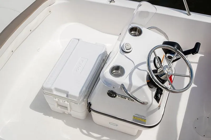 Slide: The Image of 2024 Edgewater 158CS boat console with steering wheel and cooler in white interior. - 2