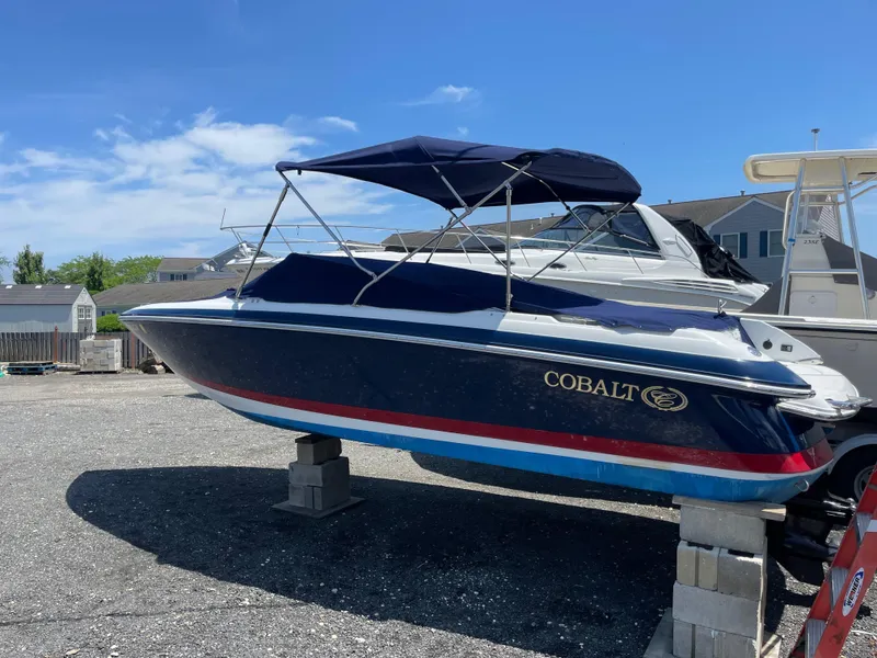 Slide: The Image of 2004 Cobalt 226 boat on blocks, blue hull, red stripe, under clear sky. - 28
