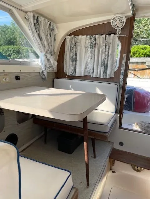 Slide: The Image of 1974 Bertram 28 Flybridge interior with dining area, featuring cushioned seating and floral curtains. - 11