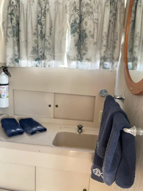 Slide: The Image of 1974 Bertram 28 Flybridge bathroom with sink, mirror, blue towels, and floral curtains. - 6