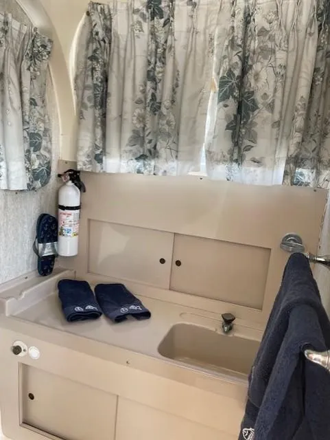 Slide: The Image of 1974 Bertram 28 Flybridge bathroom with sink, floral curtains, and fire extinguisher. - 8