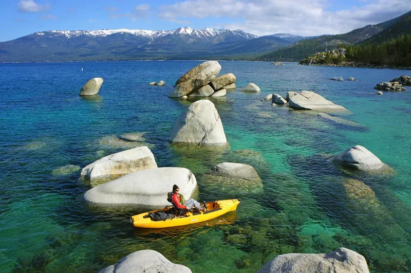 Slide: The Image of Kayaker in yellow Hobie Pro Angler 12, 2025 model, navigating clear blue lake with rocks. - 4