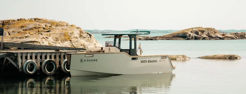 Slide: The Image of 2023 X Shore Eelex 8000 electric boat docked by rocky shoreline. - 3