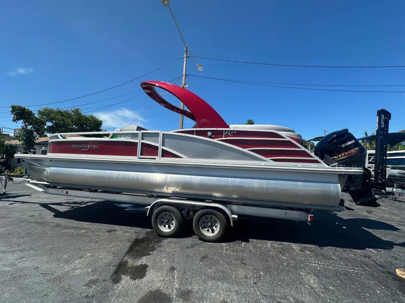 Slide: The Image of 2020 Bennington R 24 RTFBA pontoon boat on trailer, red and silver design, clear sky background. - 13