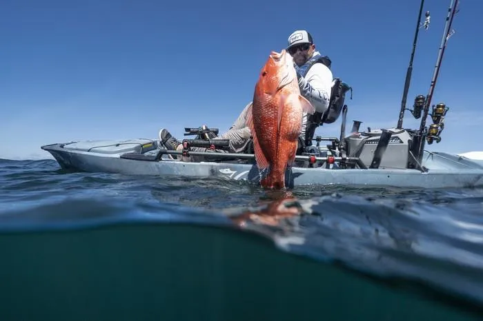 Slide: The Image of Man fishing on Hobie Pro Angler 14 kayak, holding large fish, clear blue sky. - 2