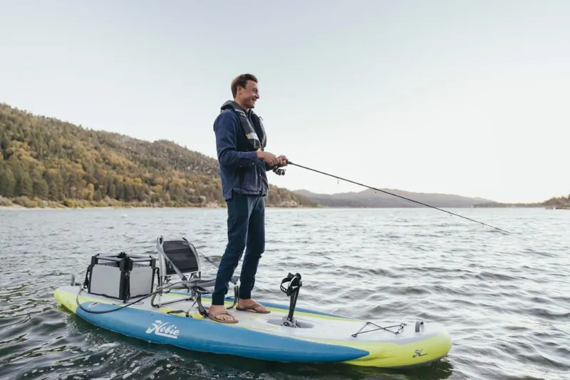 Slide: The Image of Man fishing on Hobie ITREK 11 paddleboard, 2025 model, in scenic lake setting. - 1