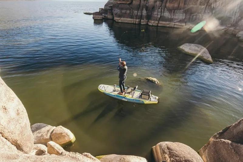 Slide: The Image of Person paddleboarding on Hobie ITREK 11, 2025 model, in rocky lake setting. - 2