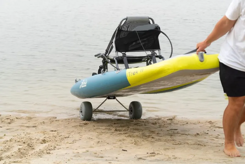 Slide: The Image of Man pulling 2025 Hobie ITREK 11 kayak on sandy beach with wheels. - 6