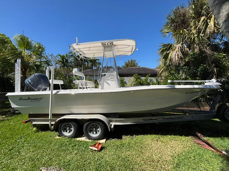 The Image of 2013 SeaHunter 24 Bay boat on trailer, parked on grass, surrounded by tropical plants. - 0