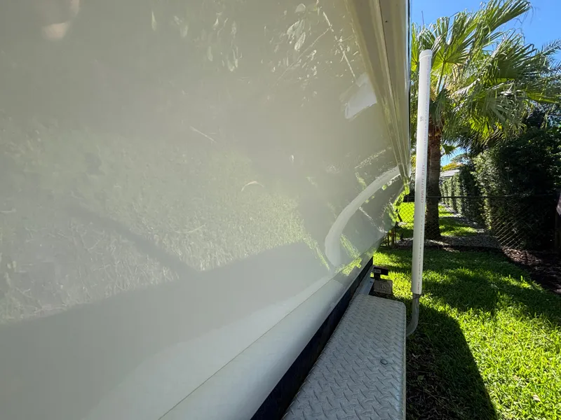 Slide: The Image of 2013 SeaHunter 24 Bay boat side view, reflecting sunlight, parked on grass near palm trees. - 9
