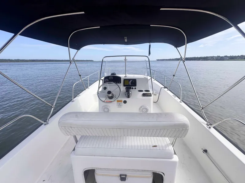 Slide: The Image of 2014 Boston Whaler 210 Montauk boat interior with steering wheel and canopy on calm water. - 12