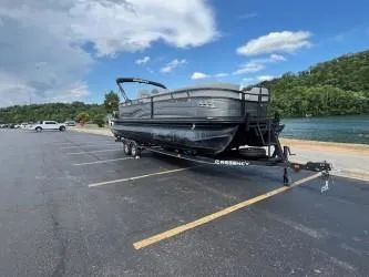 Slide: The Image of 2024 Regency 250 LE3 pontoon boat on trailer in parking lot near water. - 1