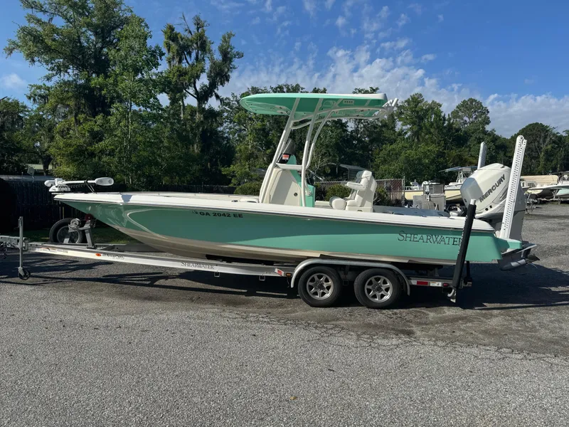 Slide: The Image of 2020 ShearWater 250 boat on trailer, parked outdoors, with trees in the background. - 3