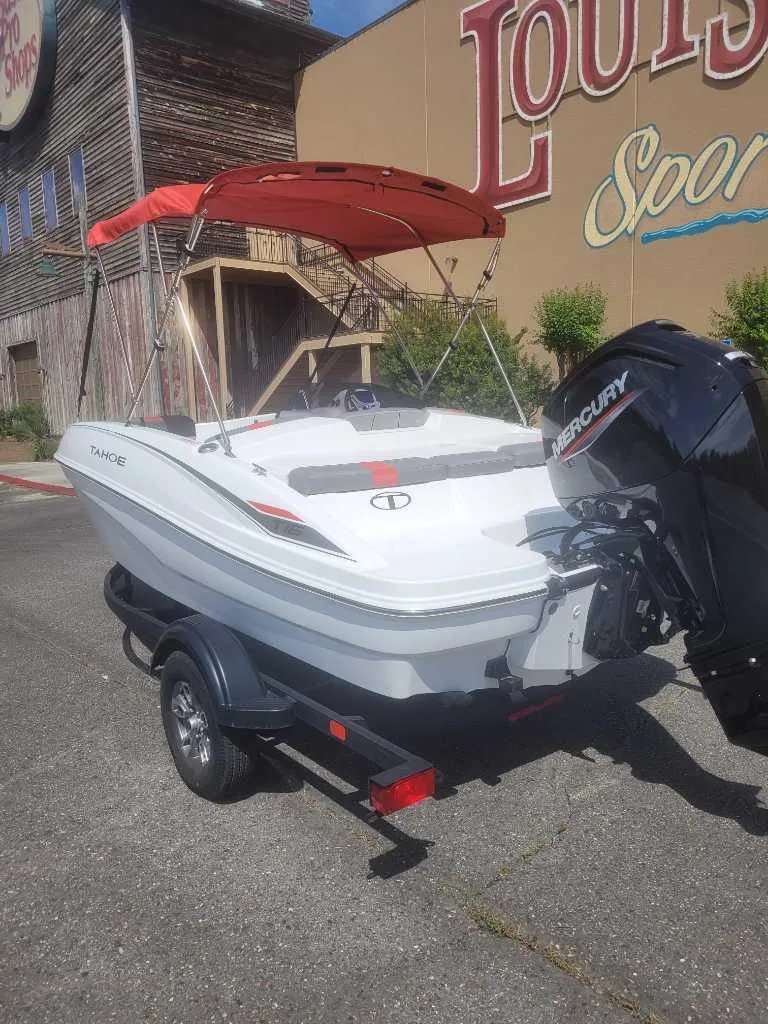 Slide: The Image of 2025 Tahoe T16 boat with Mercury engine on trailer, parked outside a sporting goods store. - 2