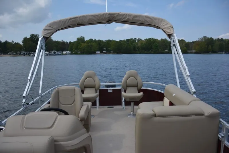 Slide: The Image of 2025 Starcraft LX 18 pontoon boat on a serene lake with beige seating and canopy. - 7