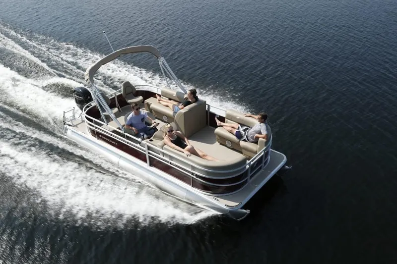 Slide: The Image of 2025 Starcraft 20 LX pontoon boat cruising on a calm lake with passengers relaxing. - 2